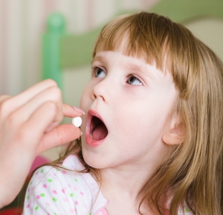 Adult putting pill into child's open mouth