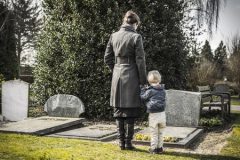 Woman and child looking at gravestone on graveyard.